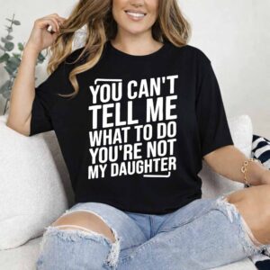 Woman sitting on a couch wearing a black shirt with large, white text expressing a humorous message.