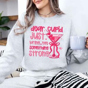 Woman in a gray sweatshirt with pink text and a martini graphic, holding a mug.